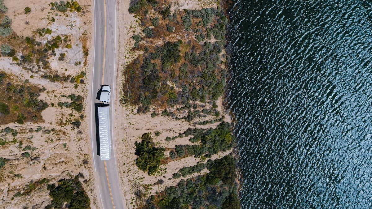 Ariel view of a truck driving down the highway near a large body of water on a sunny day.